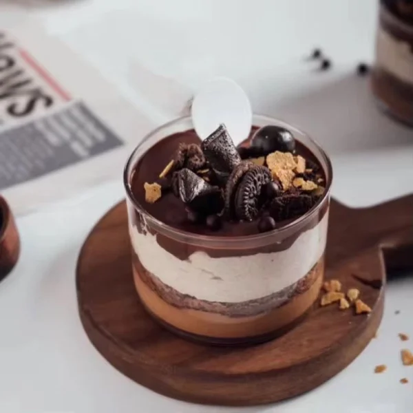An angled view of a glass dessert bowl with a vanilla, chocolate cookie dessert on trendy wooden coaster